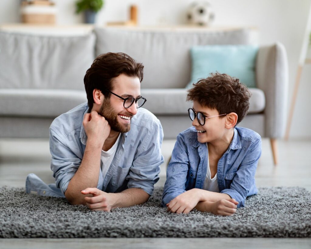 Un homme et son fils avec des lunettes, allongés sur un tapis